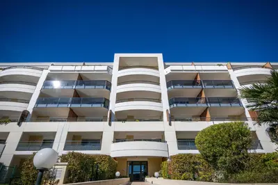 a white apartment building with trees in front of it at Nemea Appart Hotel Le Lido Cagnes sur Mer in Cagnes-sur-Mer