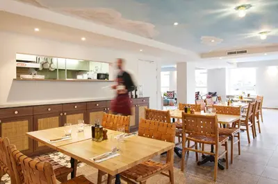 a restaurant with wooden tables and chairs and a person walking at Hotel Restaurant Isidore by Soniho in Nice