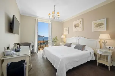 a bedroom with a white bed and a desk and a window at Hotel De La Darse in Villefranche-sur-Mer