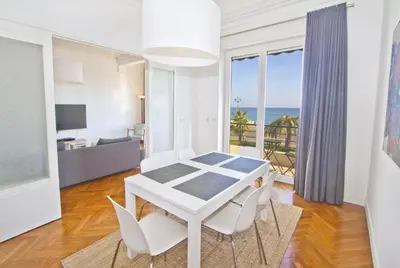 a white dining room with a table and chairs and the ocean at PROMENADE HOLIDAY - SOLEMAR PROMENADE in Nice