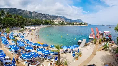 a beach with blue and white umbrellas and the ocean at Les Jasmins in Beaulieu-sur-Mer