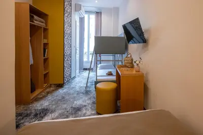 a room with a bed and a desk with a television at Hotel d'Ostende in Nice