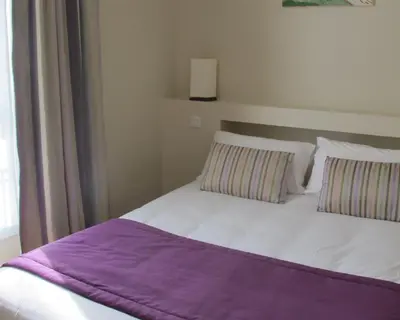 a white bed with a purple blanket on top of it at Hotel Le Havre Bleu in Beaulieu-sur-Mer