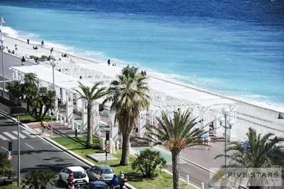 a view of a beach with a white building and palm trees at Le Majestic Promenade - Five Stars Holiday House in Nice