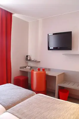 a room with two beds and a desk with a tv on the wall at Hôtel de la Fontaine in Nice