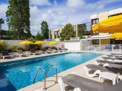 a swimming pool with chairs and umbrellas next to a building at ibis Styles Nice Cap 3000 Aéroport in Saint-Laurent-du-Var