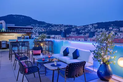a rooftop patio with tables and chairs and a pool at NH Nice in Nice