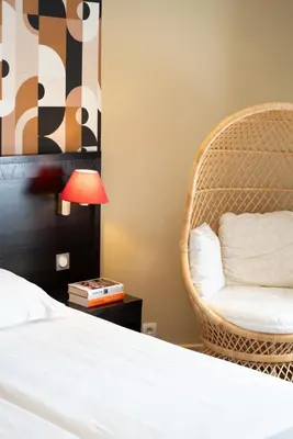 a bedroom with a bed and a wicker chair at Hôtel Comté de Nice in Beaulieu-sur-Mer