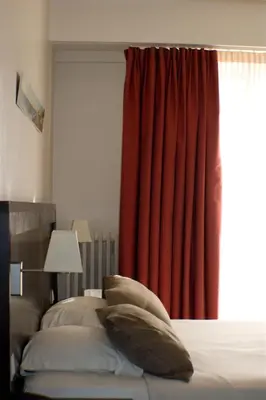 a bedroom with a bed with a red curtain at Hôtel Comté de Nice in Beaulieu-sur-Mer