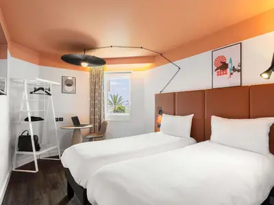 a hotel room with two beds and a desk at ibis Nice Aéroport Promenade des Anglais in Nice