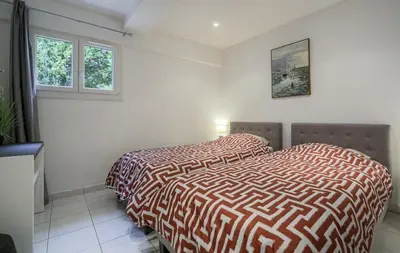 two beds in a white bedroom with two windows at Rez de villa avec beau jardin et belle vue in Saint-Laurent-du-Var