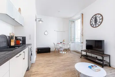 a white kitchen with a table and a clock on the wall at Bright 1 Bdr in the Old Town in Nice
