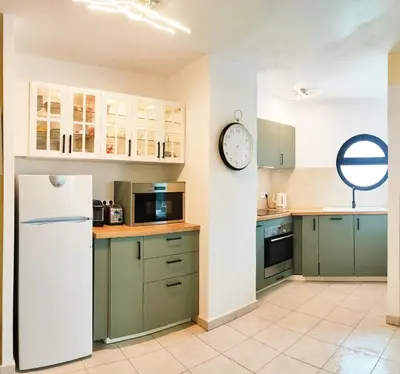 a kitchen with green cabinets and a clock on the wall at Appartement 6 personnes face à la mer in Cagnes-sur-Mer