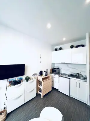 a kitchen with white cabinets and a flat screen tv at Studio Cocooning avec terrasse au calme Quartier Les Musiciens Mer à 7 minutes à pieds in Nice