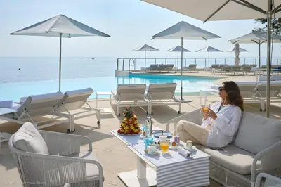 a woman sitting on a couch next to a pool at Hotel Cap Estel in Èze