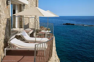 a balcony with chairs and an umbrella and the water at Hotel Cap Estel in Èze