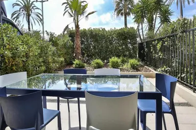 a glass table and chairs on a patio with palm trees at Sublime Appartement Promenade des Anglais RDJ in Nice