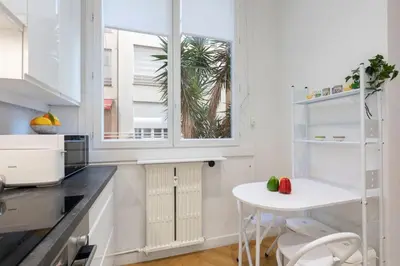 a white kitchen with a table and a window at Promenade, 2pièces chic et clim avec terrasse Location éligible au Bail Mobilité Mobility Lease in Nice