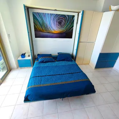 a bedroom with a blue bed with a painting on the wall at Grand studio bord de mer- accès direct aux plages in Saint-Laurent-du-Var