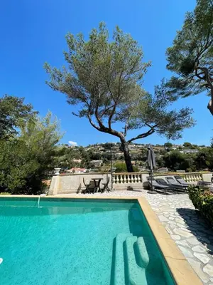 a swimming pool with a tree in the background at appartement bas de villa avec piscine privée partagée proche bord de mer in Cagnes-sur-Mer