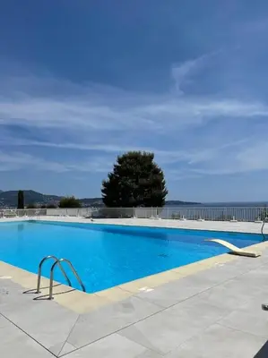 a large blue swimming pool with a tree in the background at Exceptional sea view, tennis, parking, WiFi in Nice