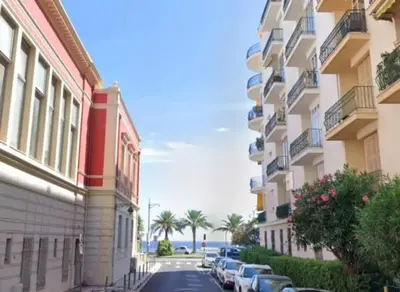 a street between two buildings with parked cars and the ocean at Nice, Seaside apartment in Nice