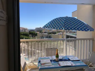 a table with a bottle of wine and an umbrella on a balcony at Charmant studio à Cros de Cagnes in Cagnes-sur-Mer