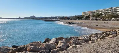 a beach with rocks in the water and a building at 2 pièces calme et fonctionnel in Cagnes-sur-Mer