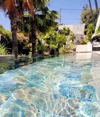 a swimming pool with blue water and palm trees at COTTAGE MARIN avec VUE MER in Nice